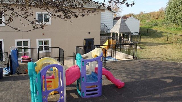 Playground with colorful slides, fenced area, and beige building in the background.