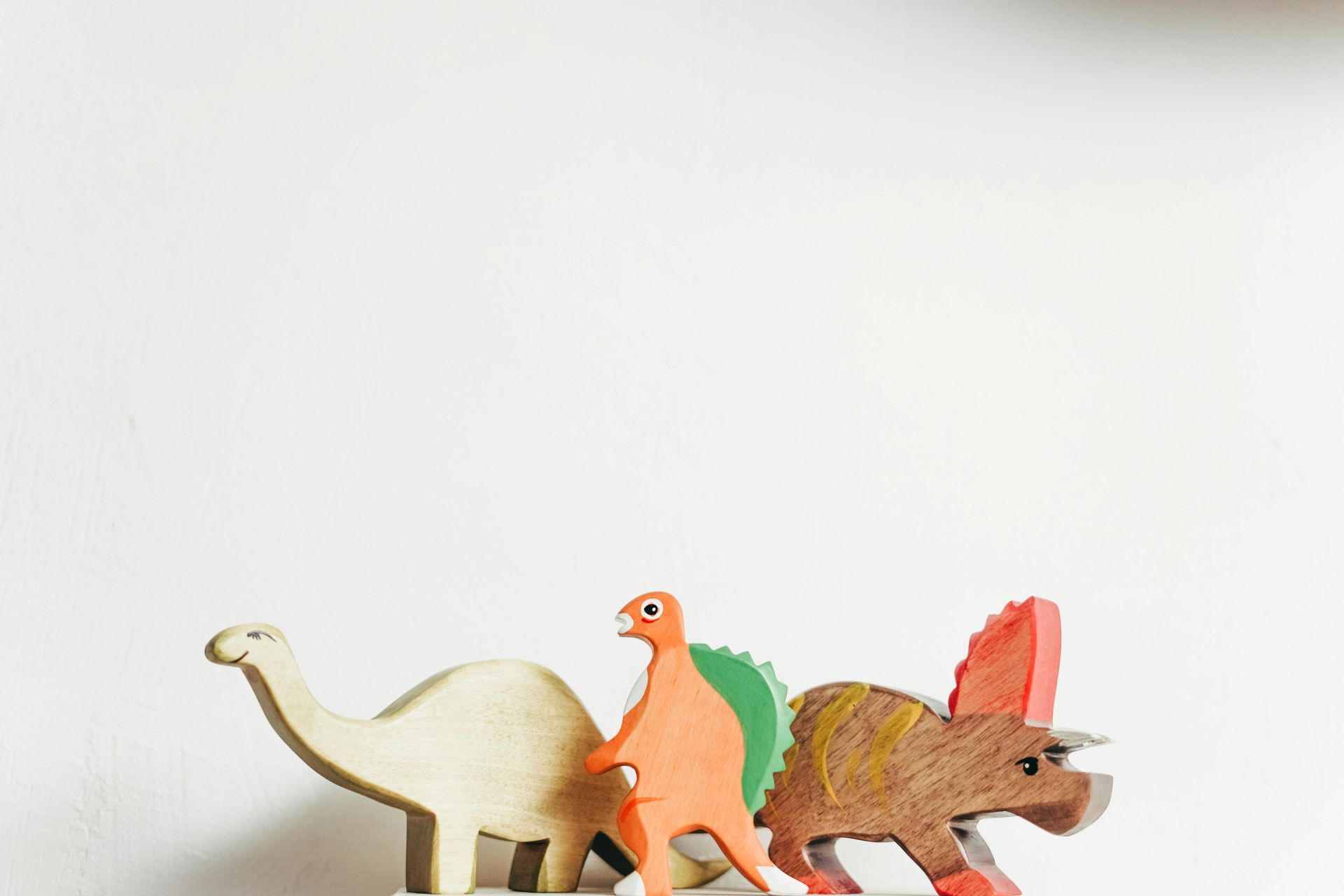 Three wooden dinosaur toys of varying colors on a white surface.