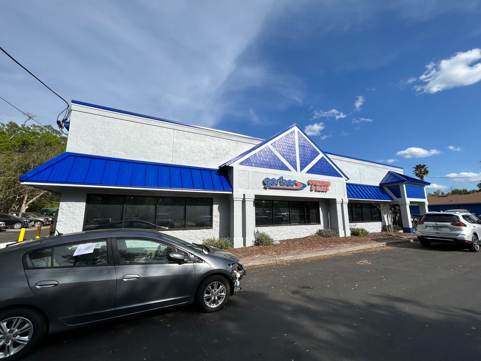 A gray car is parked in front of a white building with a blue awning.