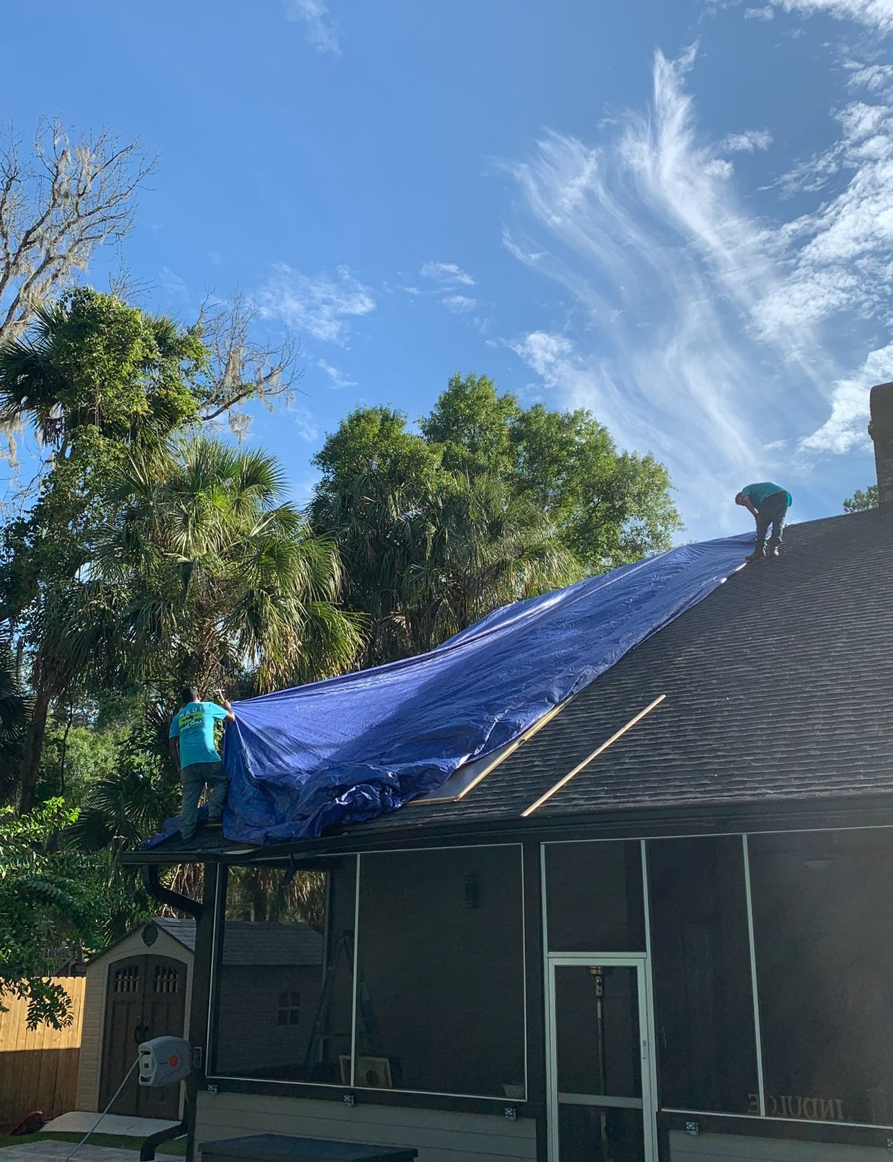 A man is covering the roof of a house with a blue tarp.