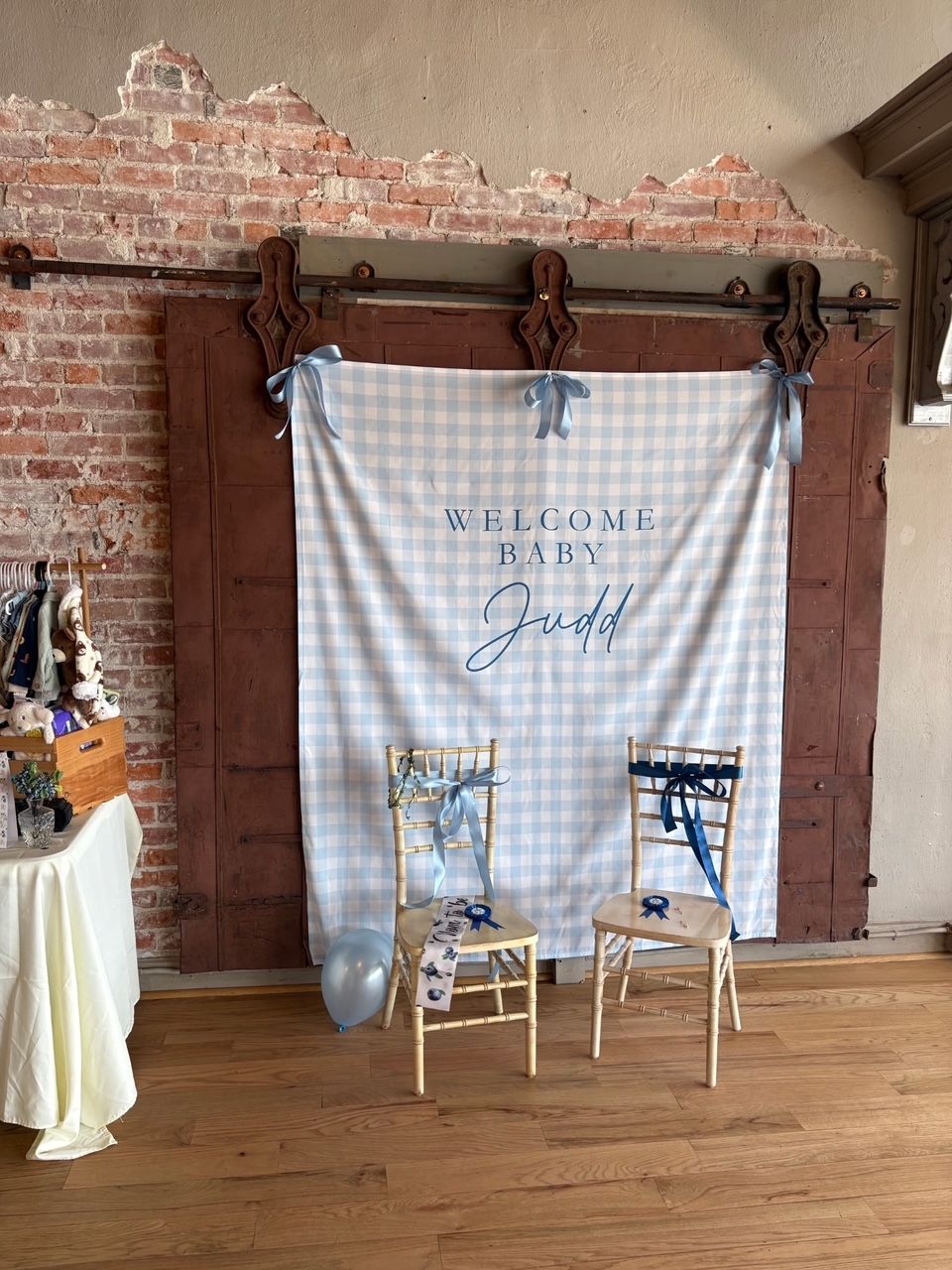 Rustic wedding welcome backdrop with blue plaid drape, two chairs, and exposed brick wall