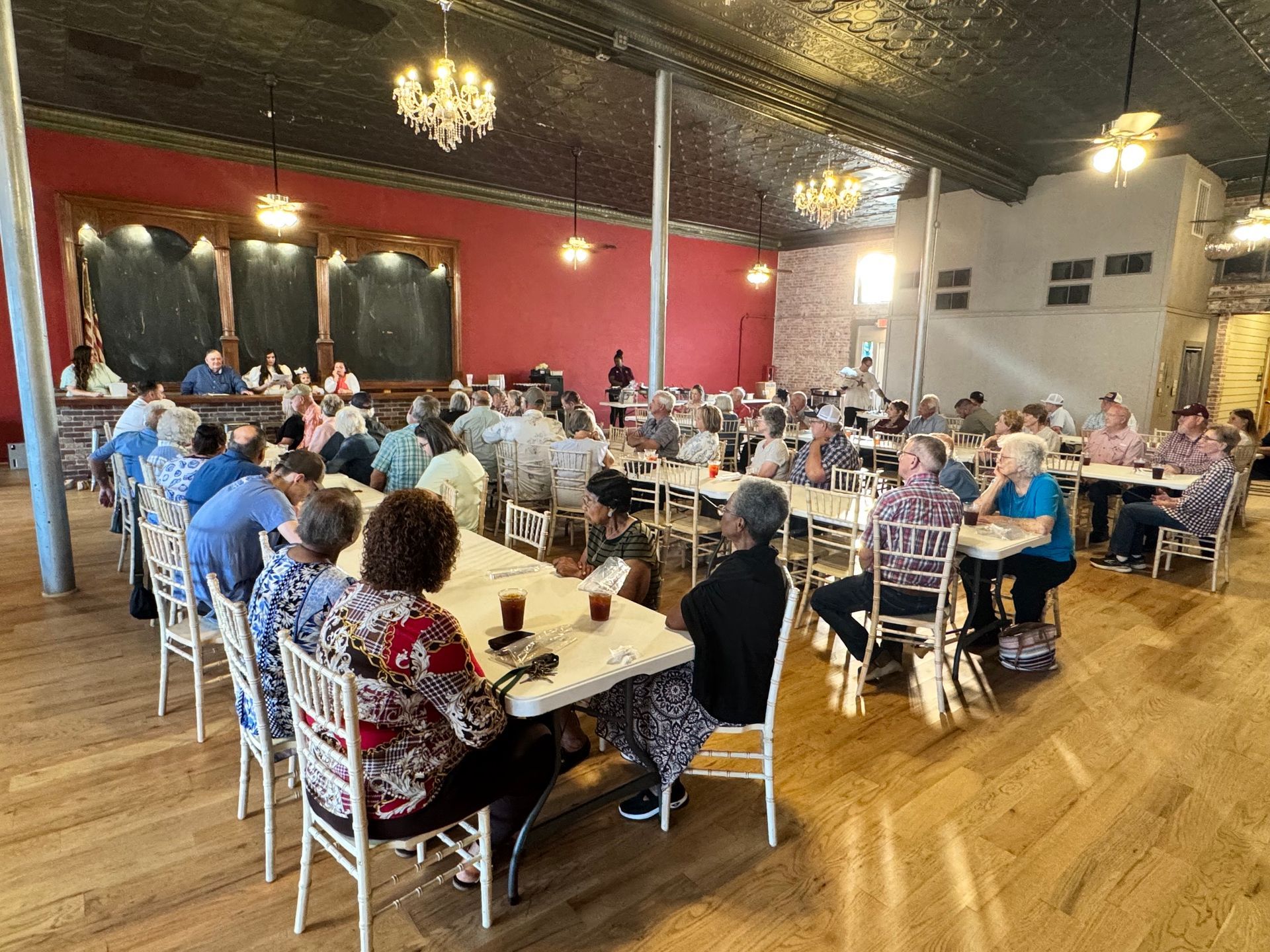 Banquet hall with many people seated at long tables for a social gathering, under chandeliers and warm lighting