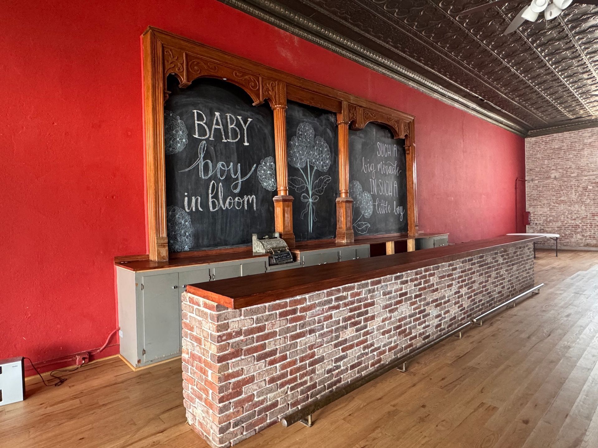 Red-walled bar with chalkboard signs and a brick counter in a wooden-floored room