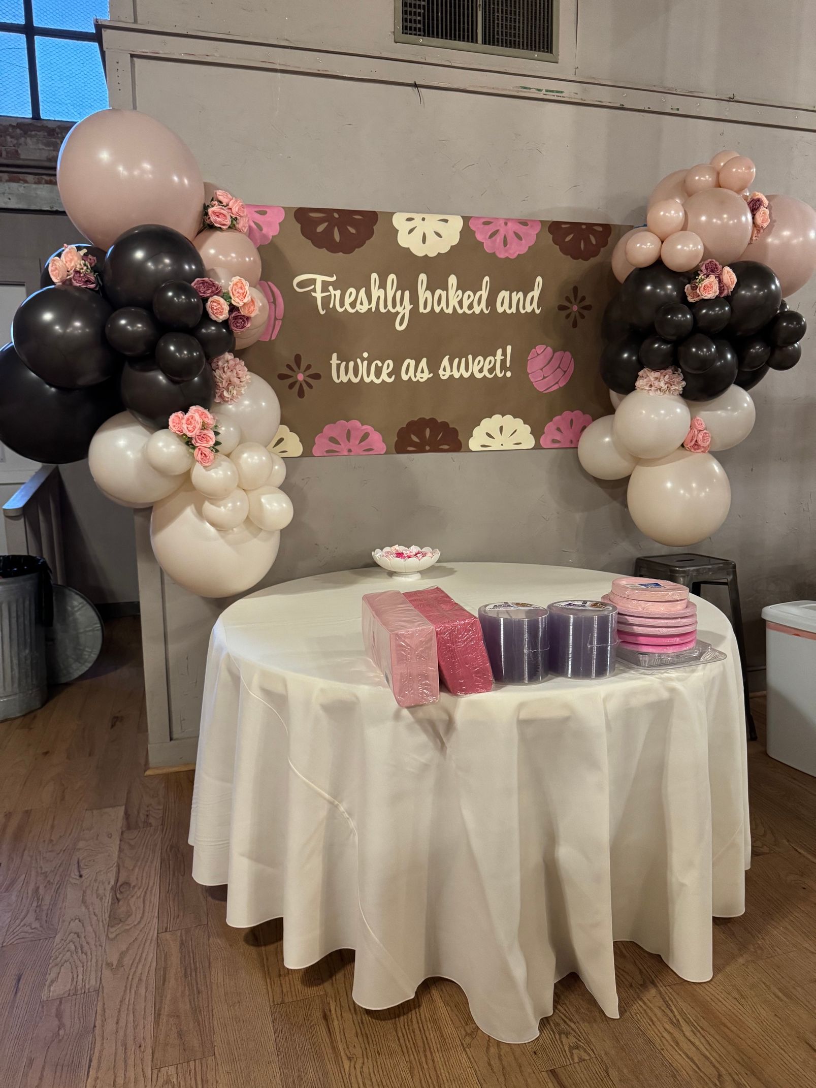 Birthday dessert table with pink, black, and beige balloon decorations and a “First birthday” banner