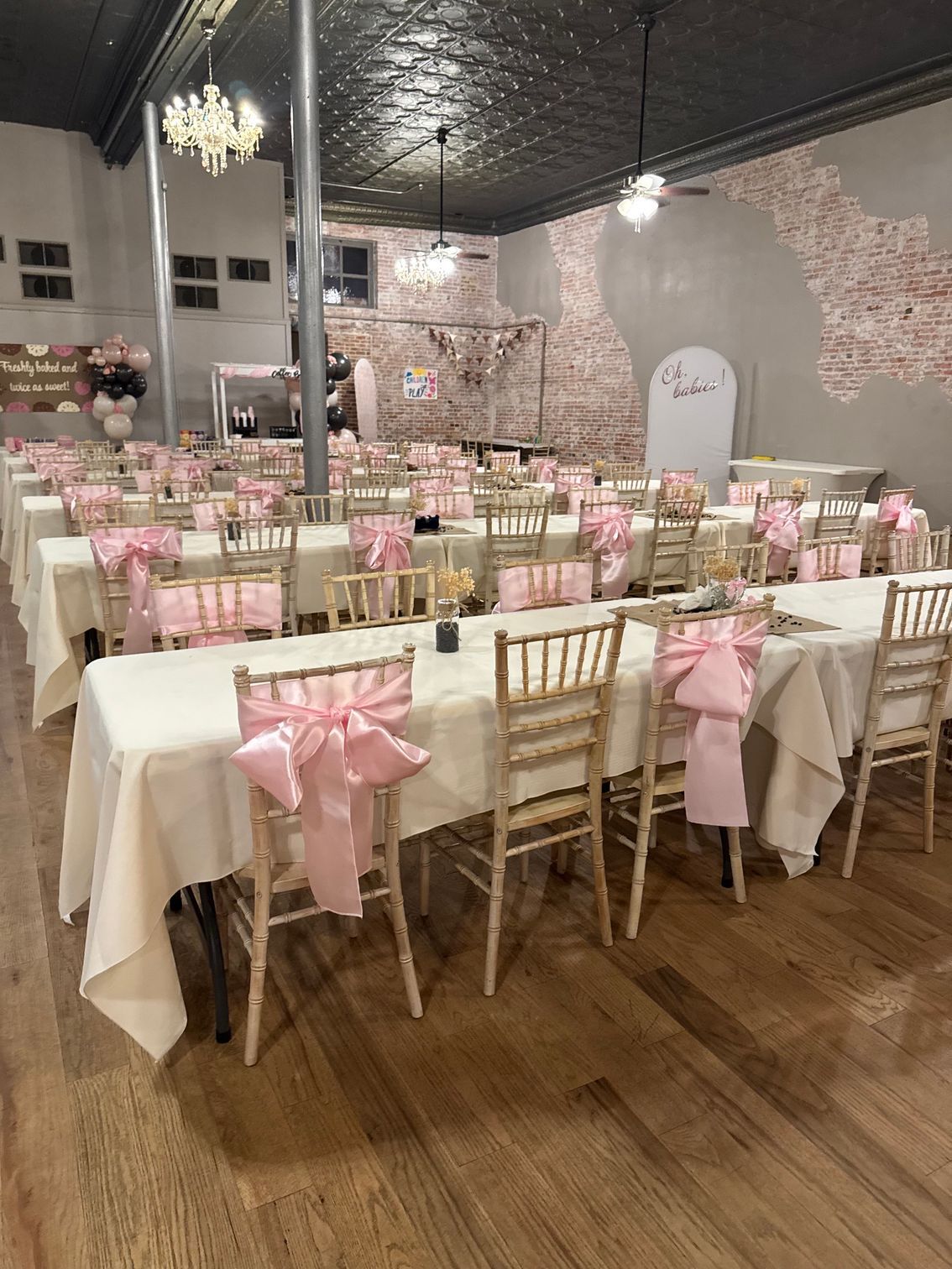 Decorated banquet hall with long tables, gold chairs, and pink bows set for an event