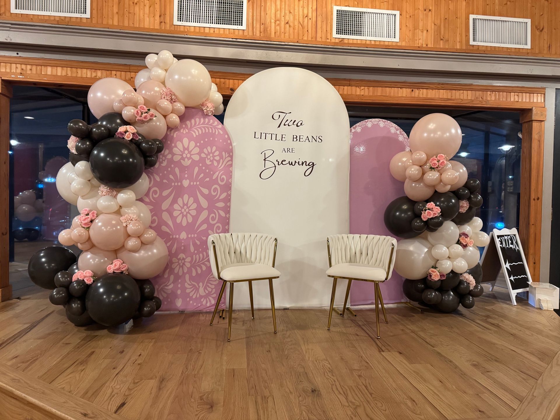 Pastel pink and black balloon backdrop with two chairs and a sign for a bridal shower