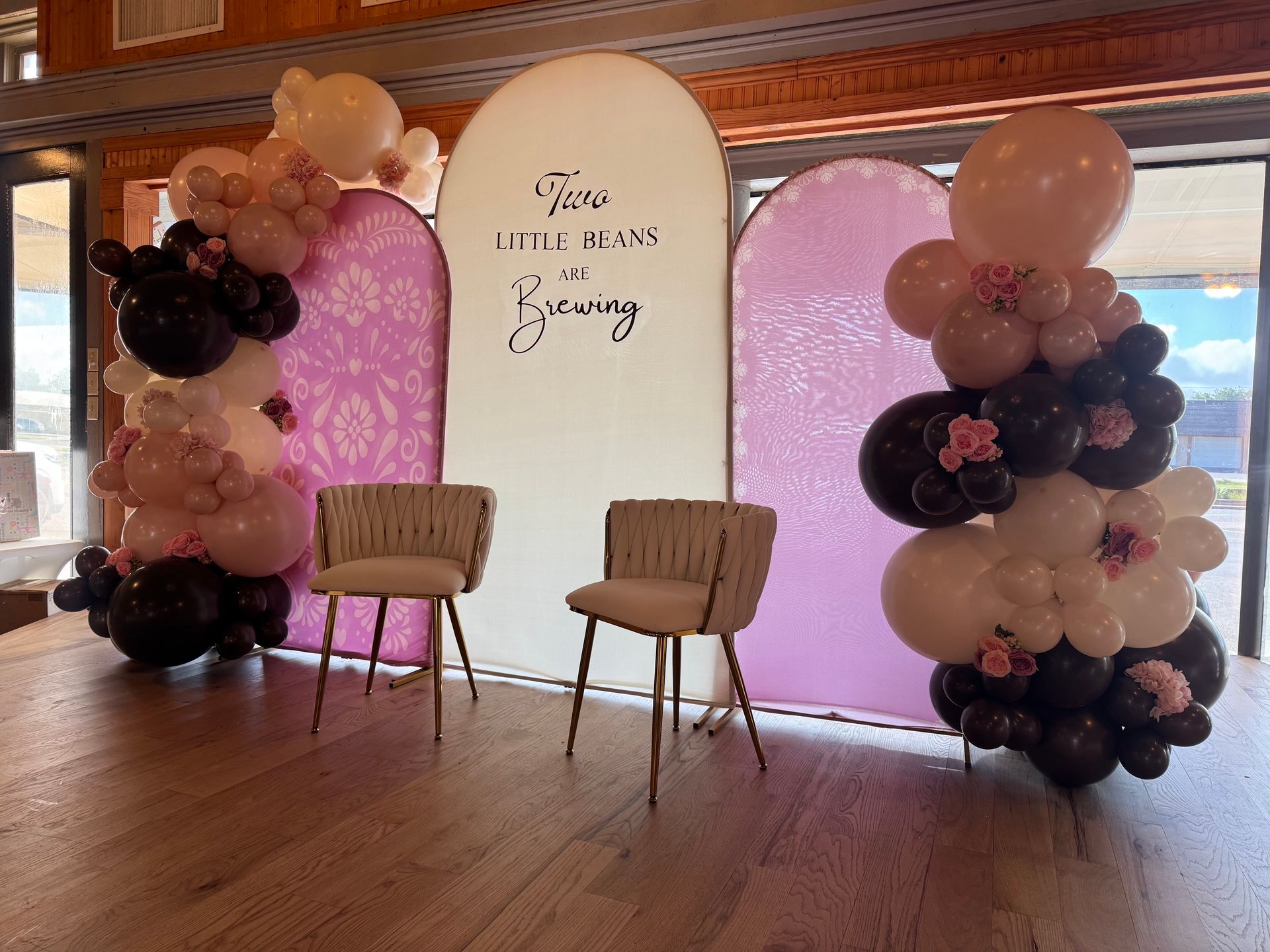 Birthday party backdrop with pink balloons, two chairs, and a white sign panel in a wooden hall