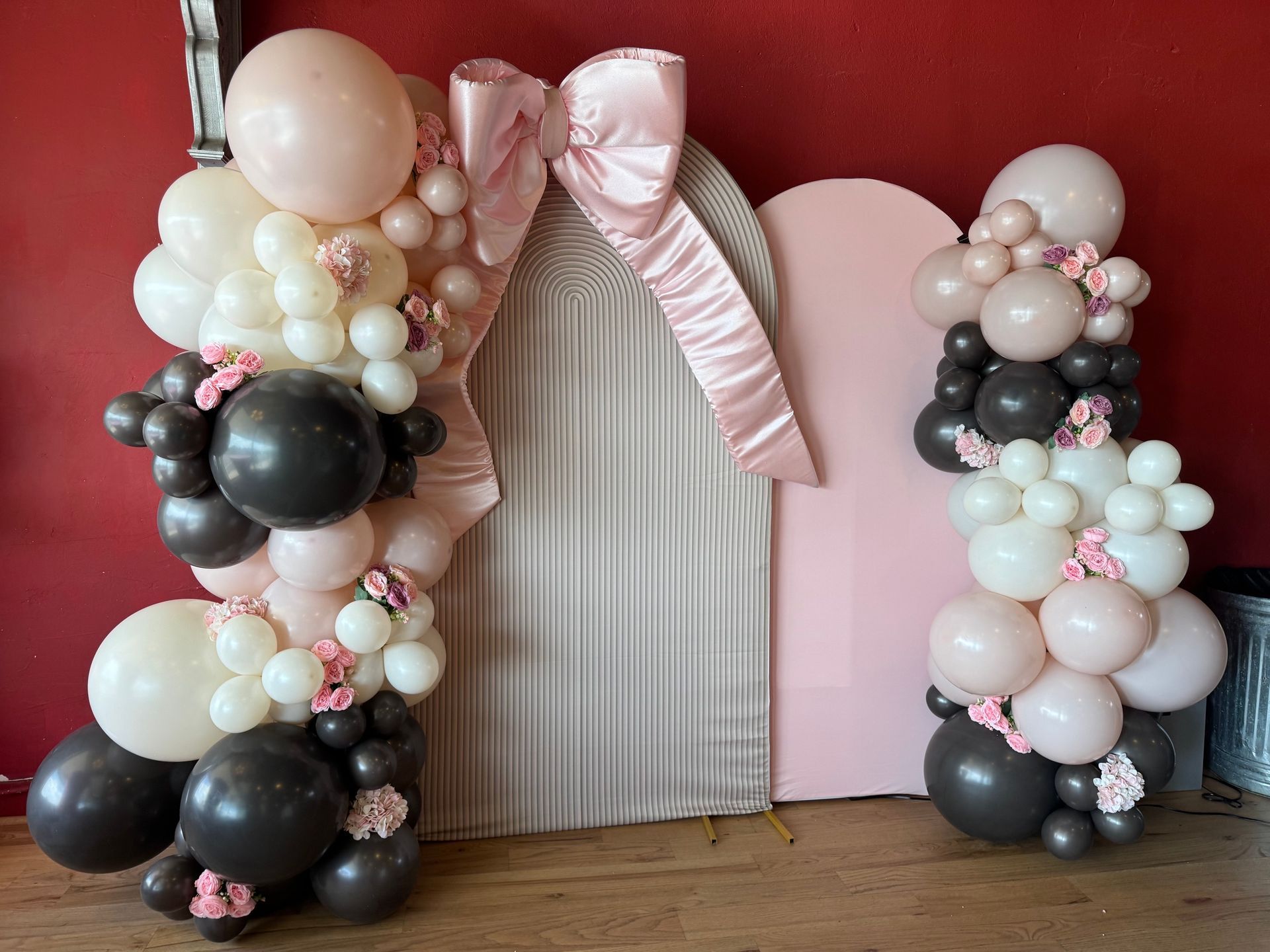 Balloon arch with pink, white, black, and gray balloons framing a draped doorway against a red wall