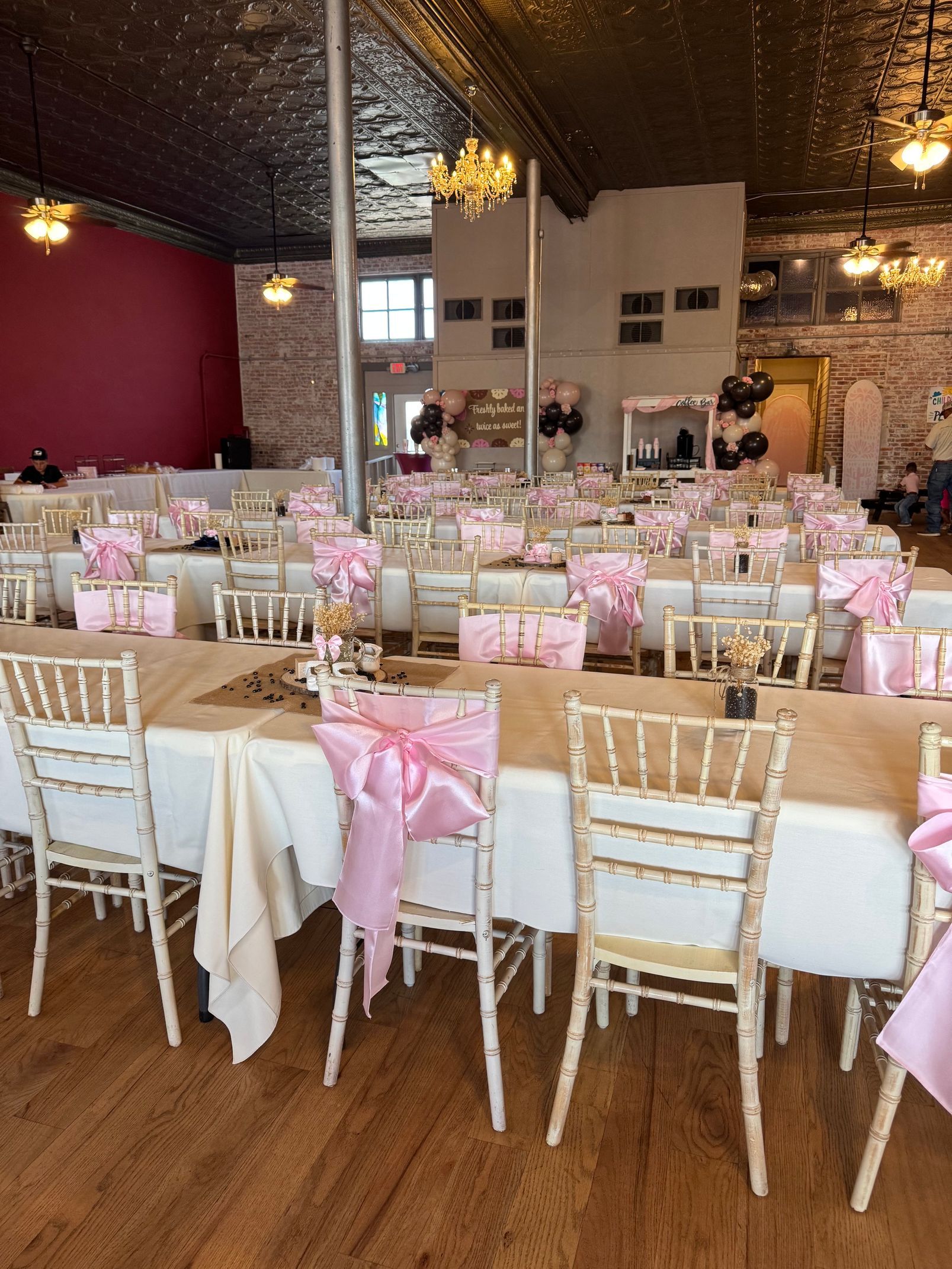 Decorated banquet hall with long tables, pink accents, and gold chairs set for an event