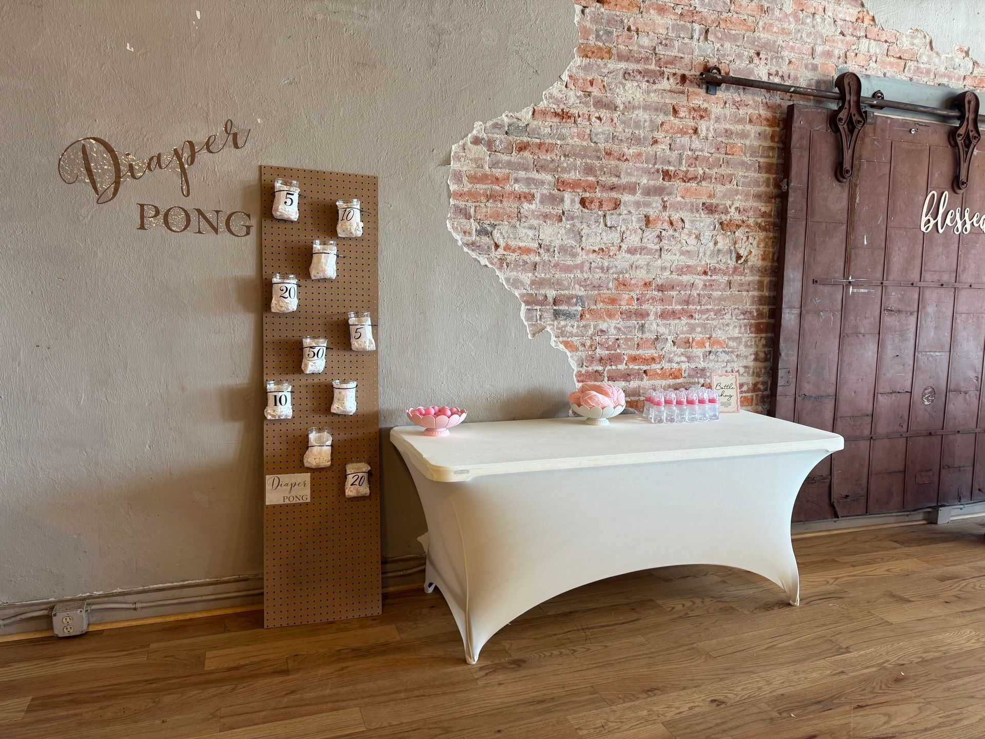 Decorated event table with white cloth, wall sign, and a hanging mug display in a rustic indoor setting