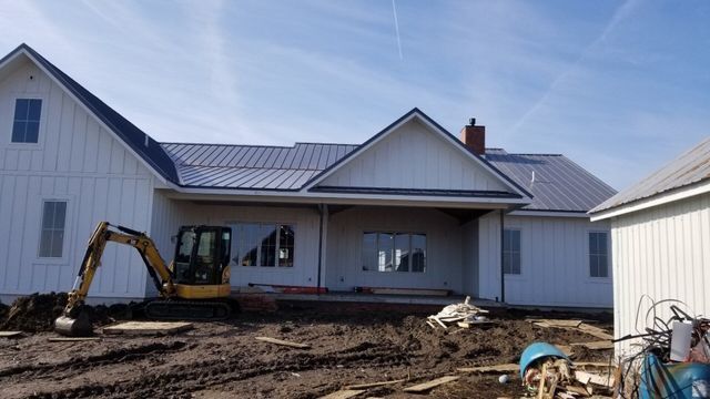 White house under construction with excavator and dirt in front yard under blue sky