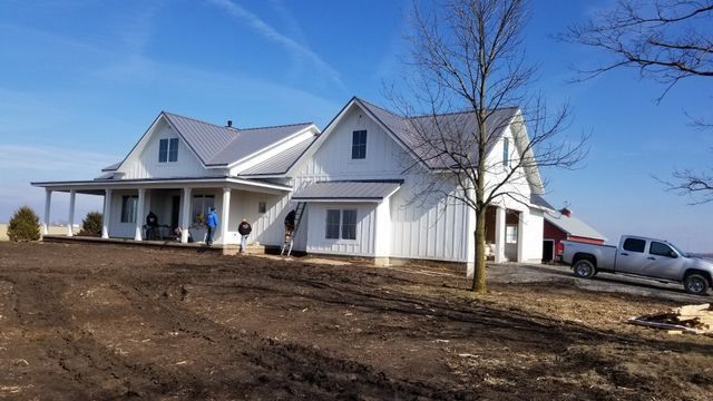 White farmhouse with porch and attached garage on a bare lot under a clear blue sky