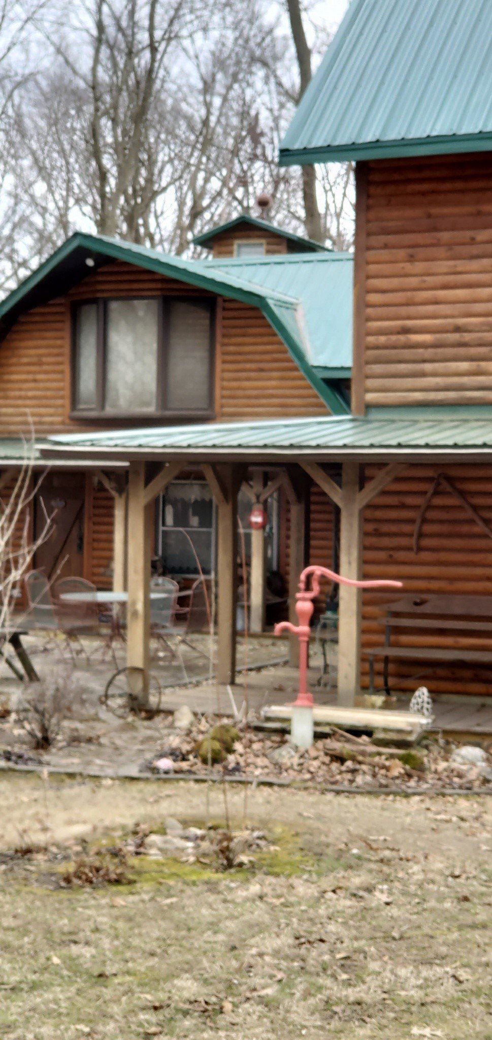 Rustic wooden cabin with green metal roof and porch, seen from the yard