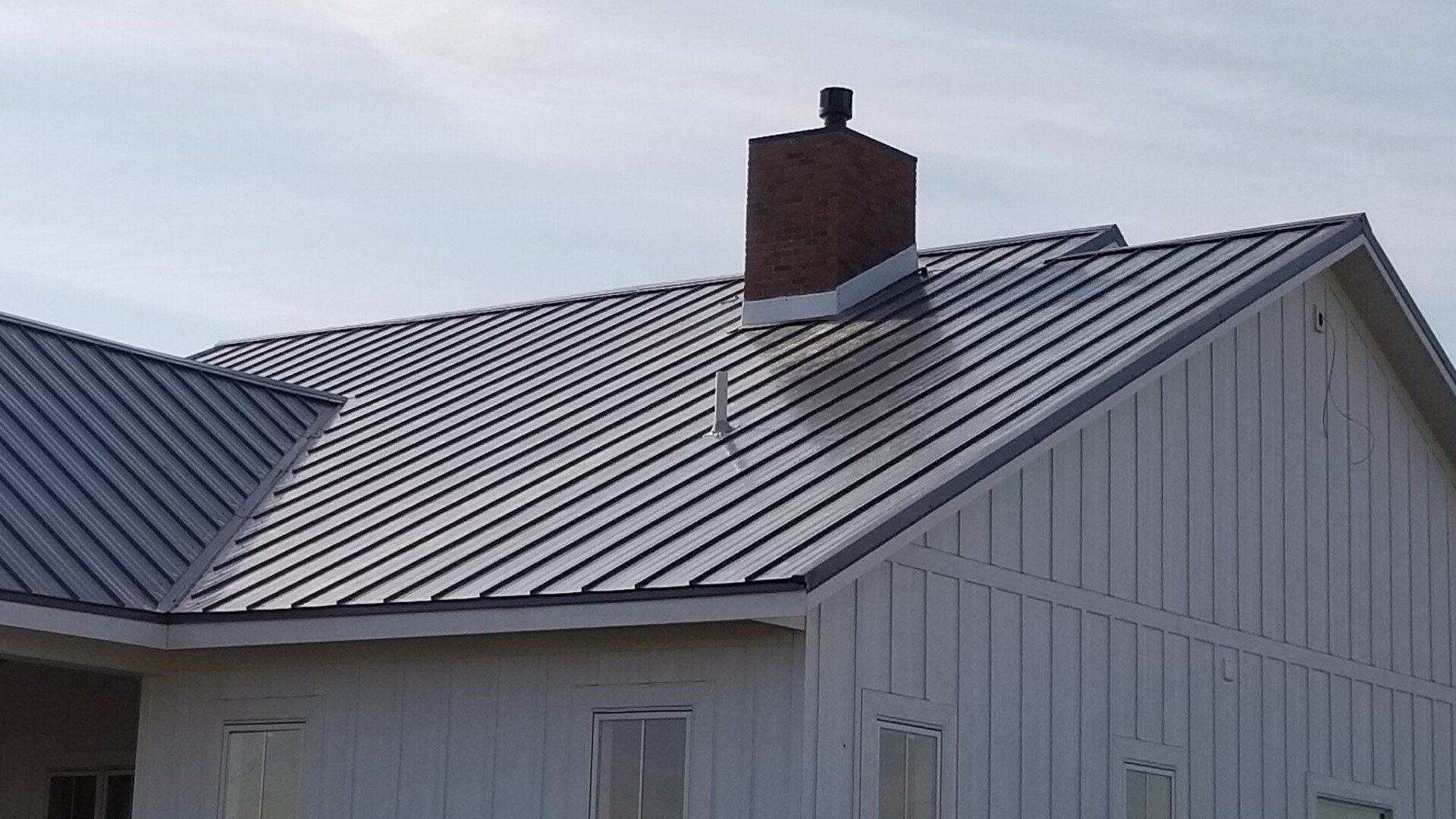 White metal-roofed house with a brick chimney and white siding under a pale sky
