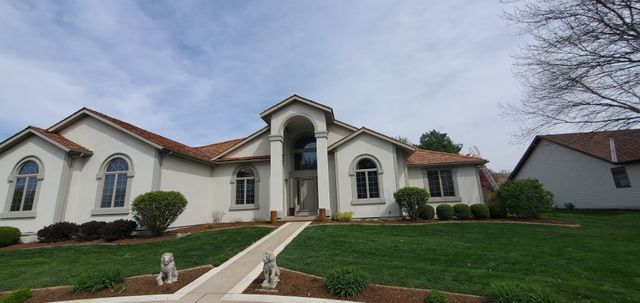 Large cream-colored suburban house with arched windows, front walkway, and manicured green lawn