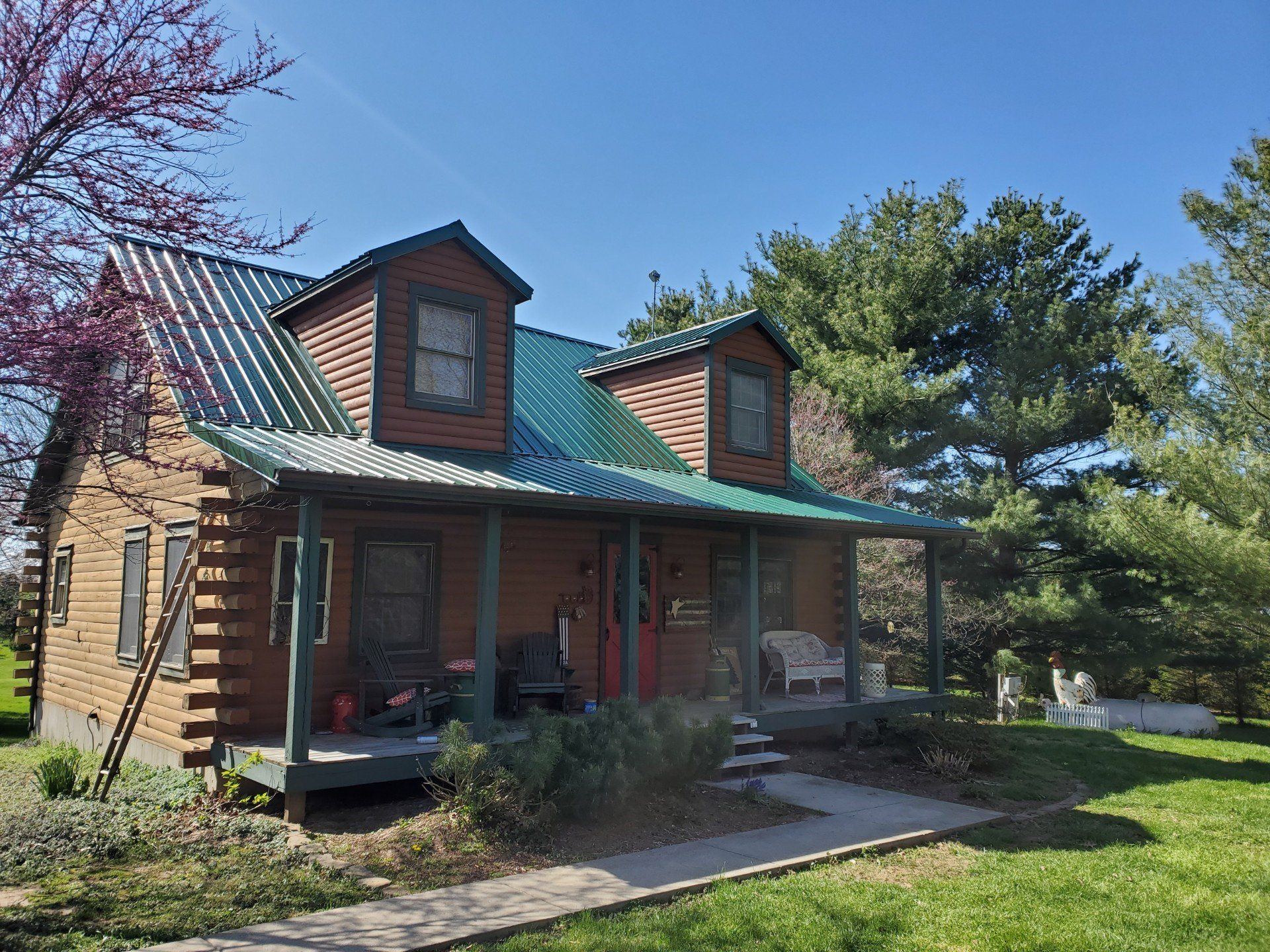 Brick house with green metal roof and dormers, set among trees on a sunny day