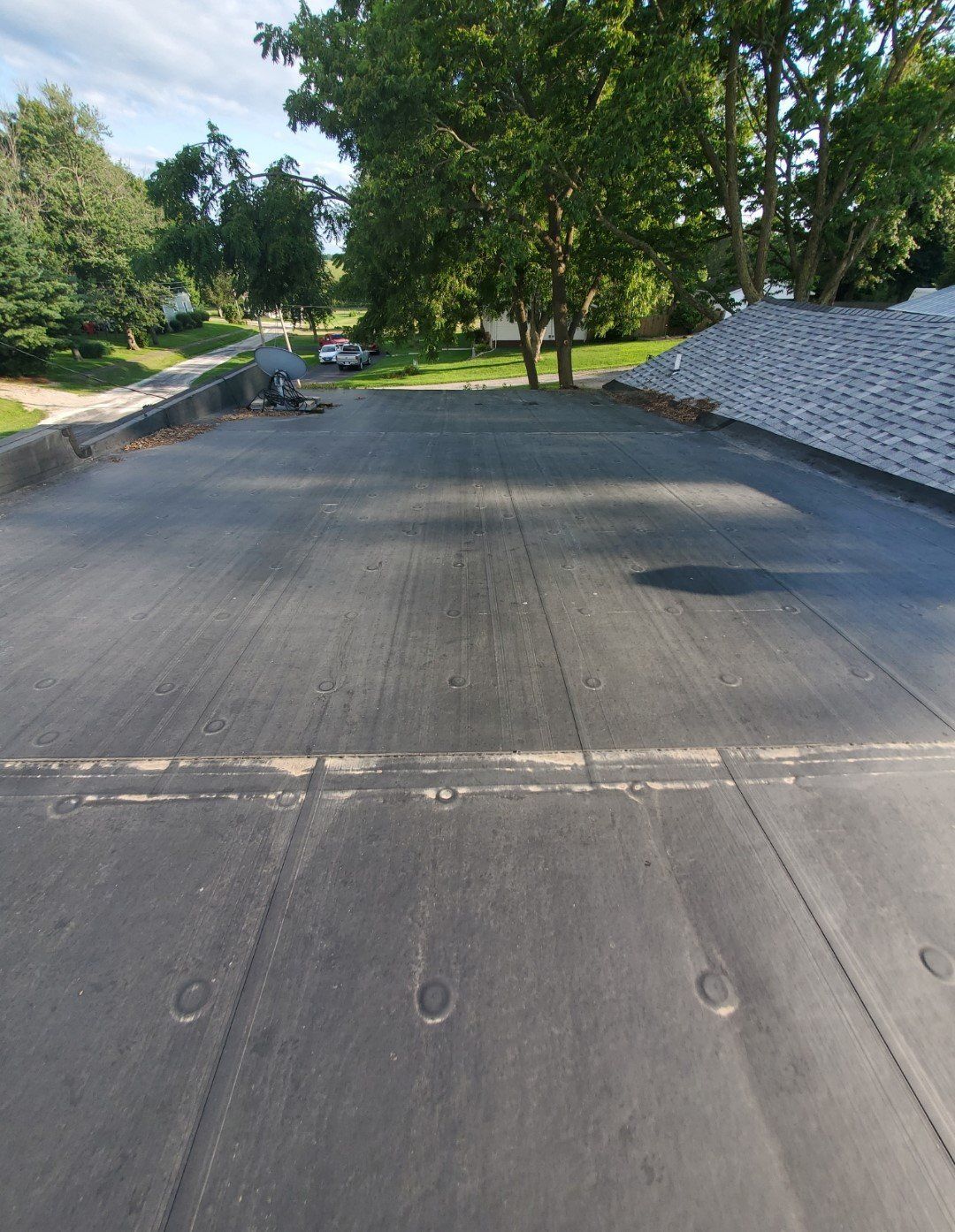 Freshly paved road in a tree-lined area, with gravel piles along the sides and a parked truck in the distance.