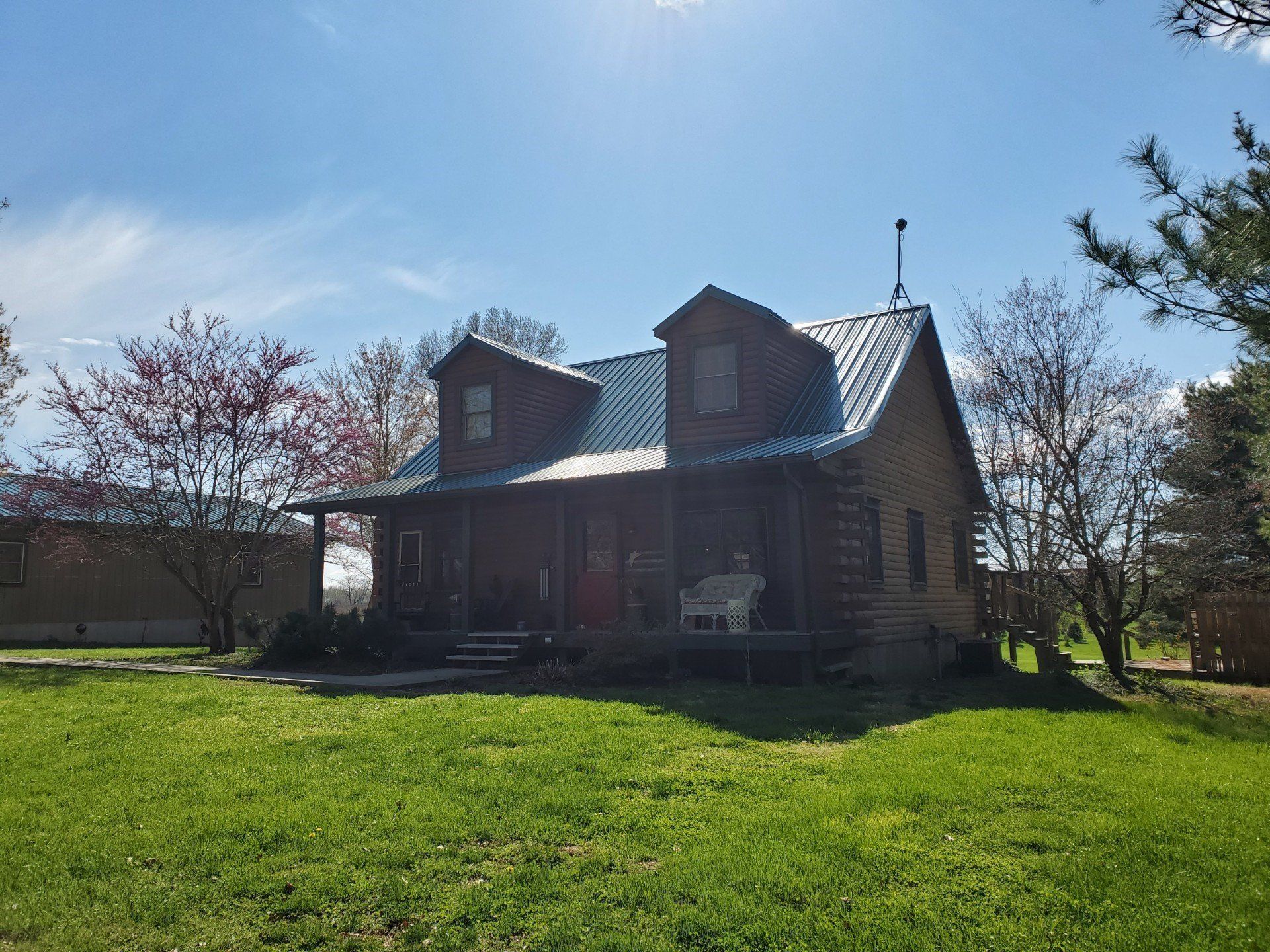 Small brick house with a green roof on a sunny lawn, surrounded by trees and blue sky.