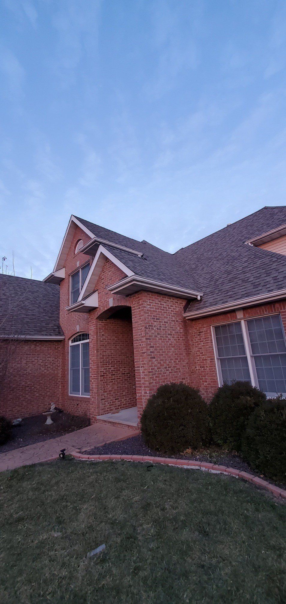 Brick house exterior with gabled roof, front entry, and lawn at dusk