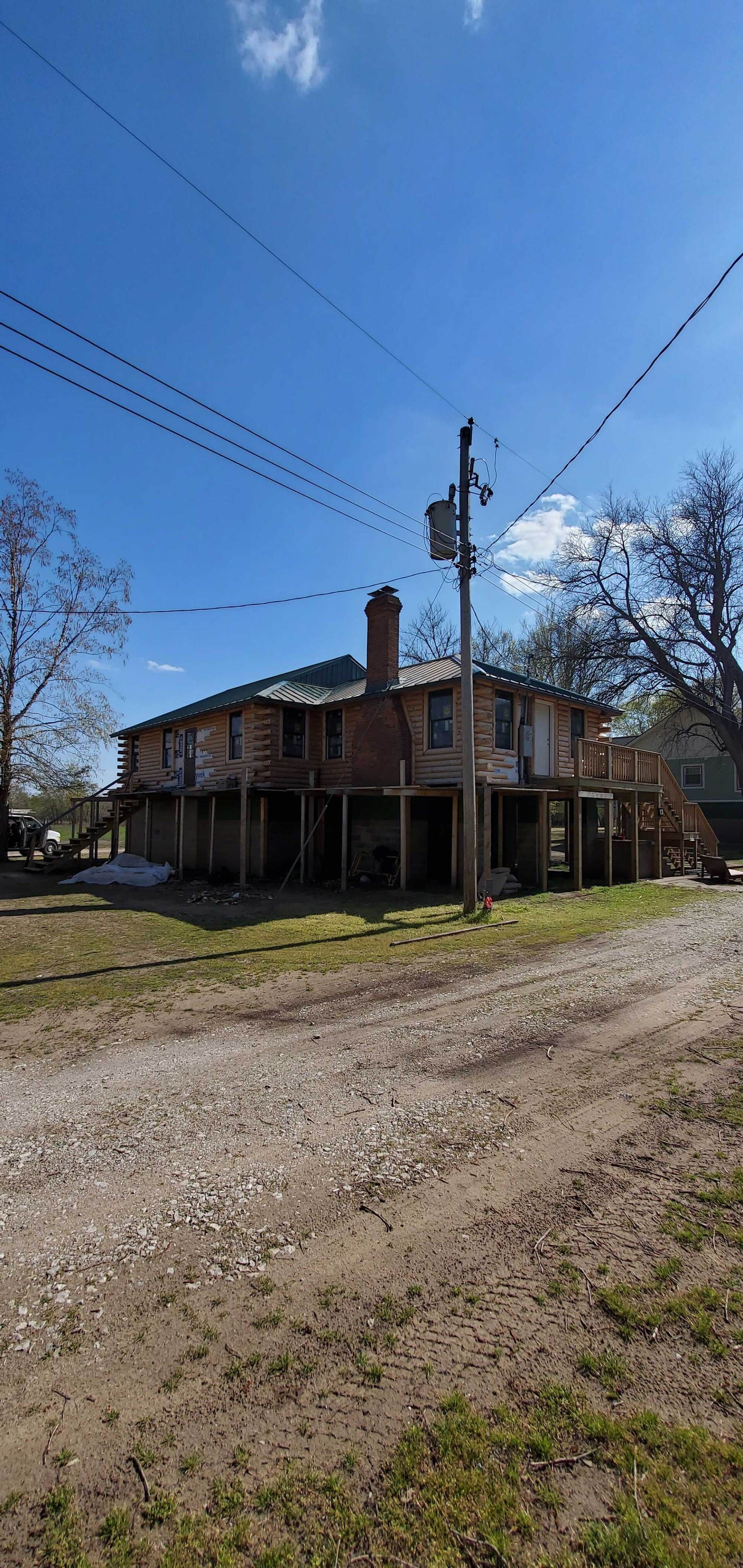 Rural house with a porch beside a gravel road under a clear blue sky, with power lines overhead