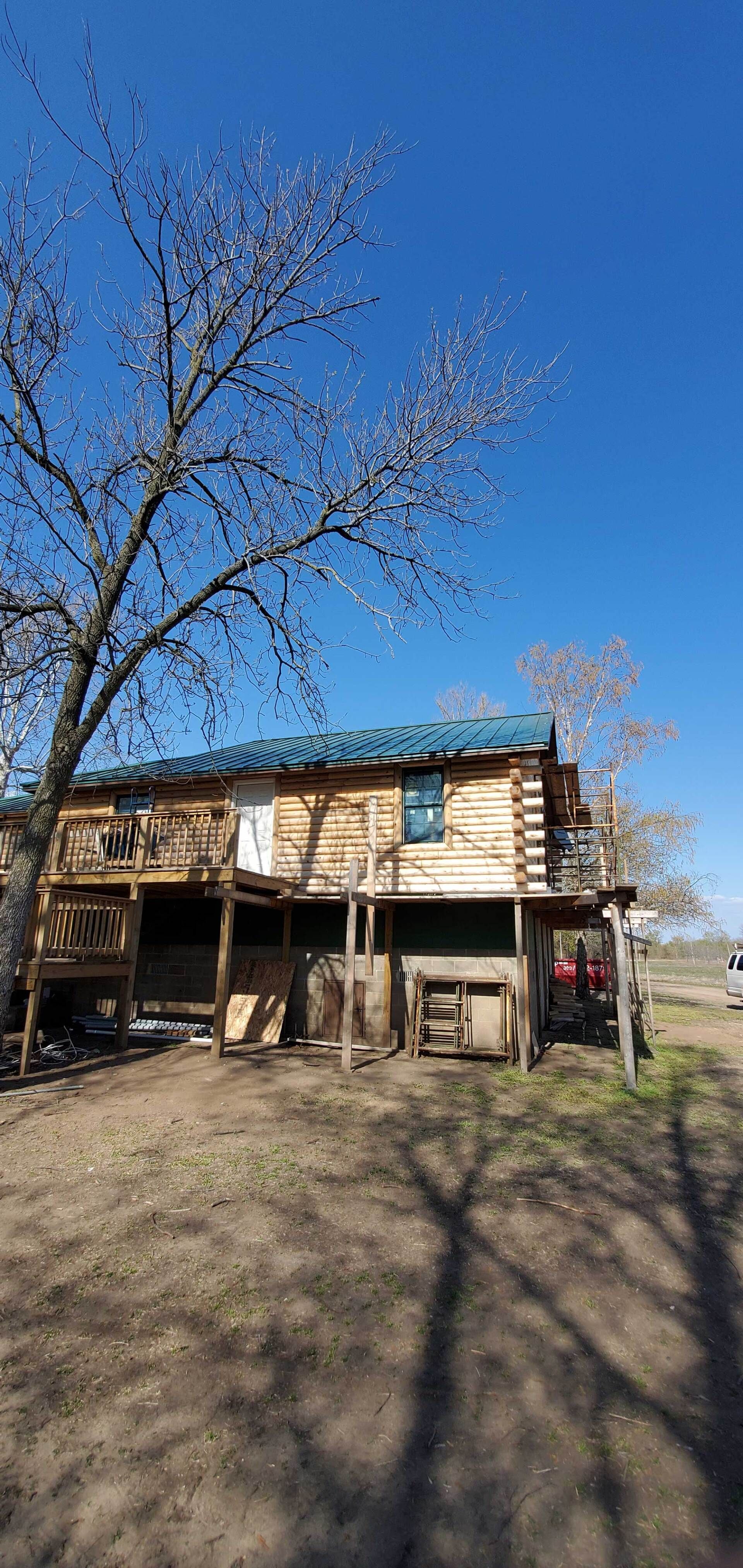 Rural wooden shed under leafless trees on a clear blue day, with a dirt yard in front