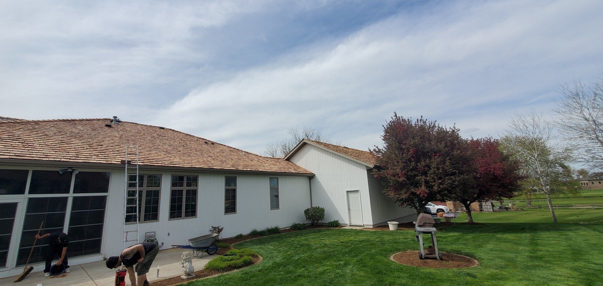 White house with damaged roof and windows, lawn and blossoming tree under a cloudy sky