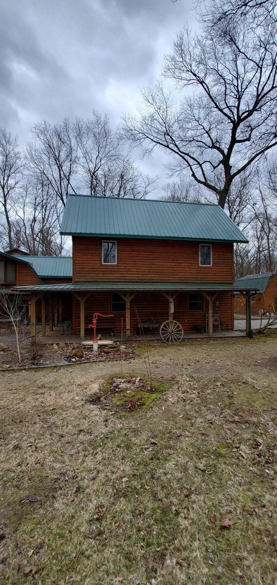Red brick house with a covered porch in a leafless yard under a cloudy sky