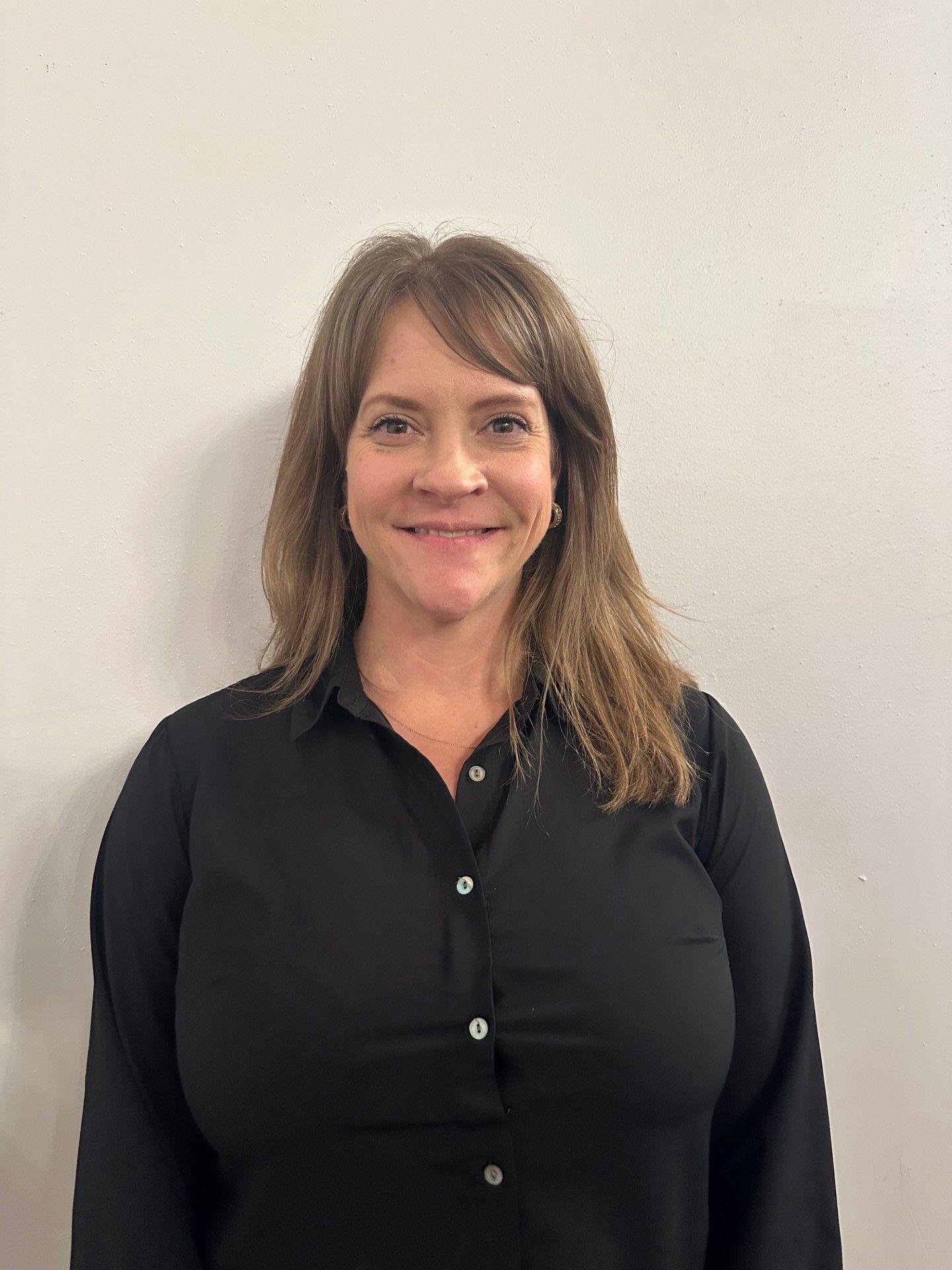 A woman in a black shirt is smiling and standing in front of a white wall.