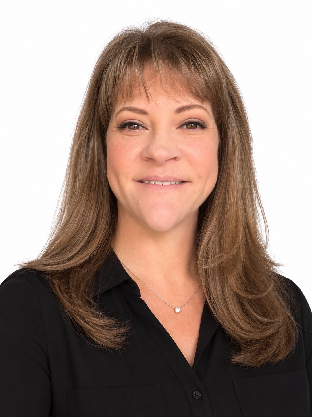 A woman in a black shirt is smiling and standing in front of a white wall.