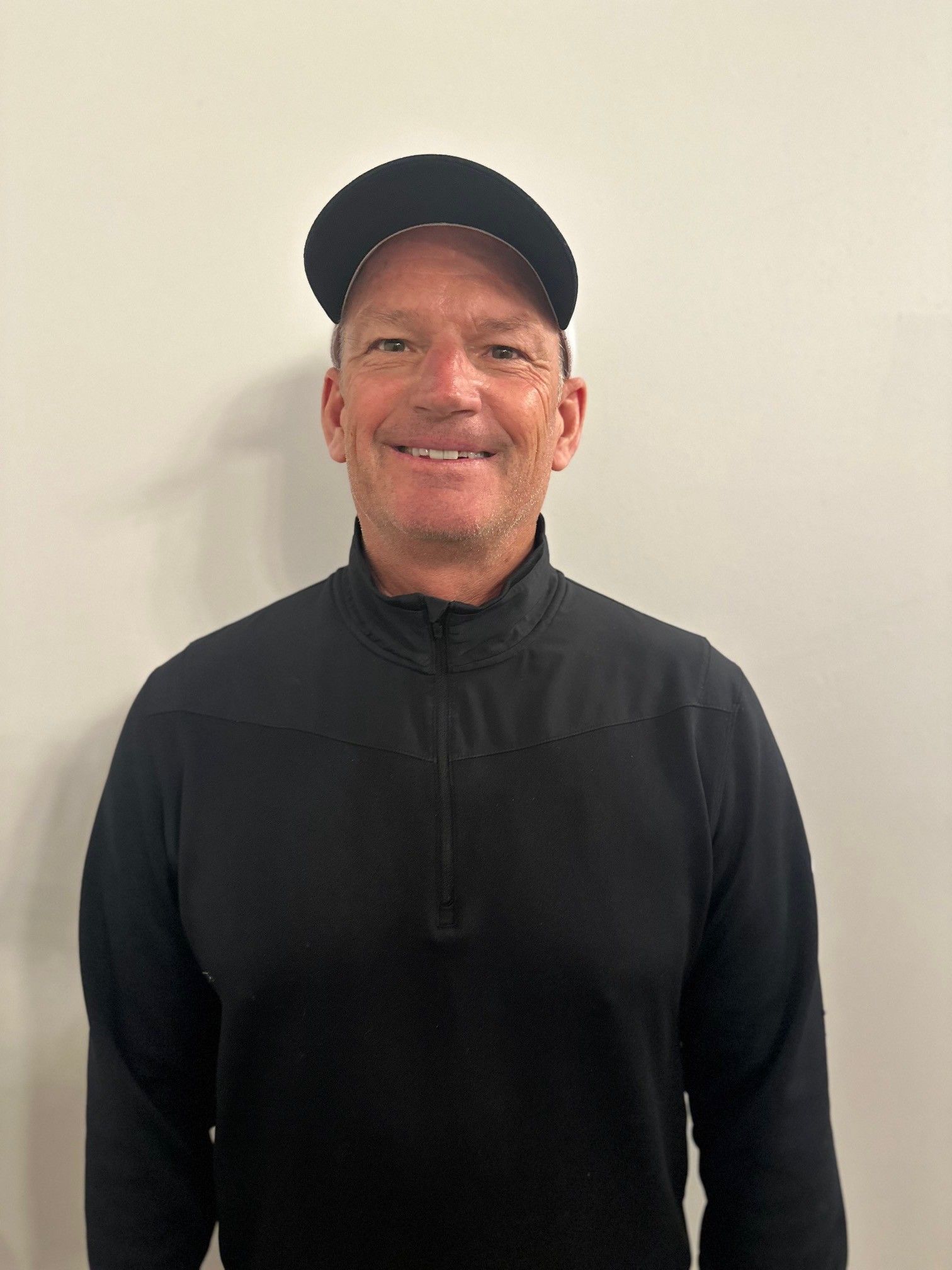A man wearing a hat and a black sweater is smiling for the camera.
