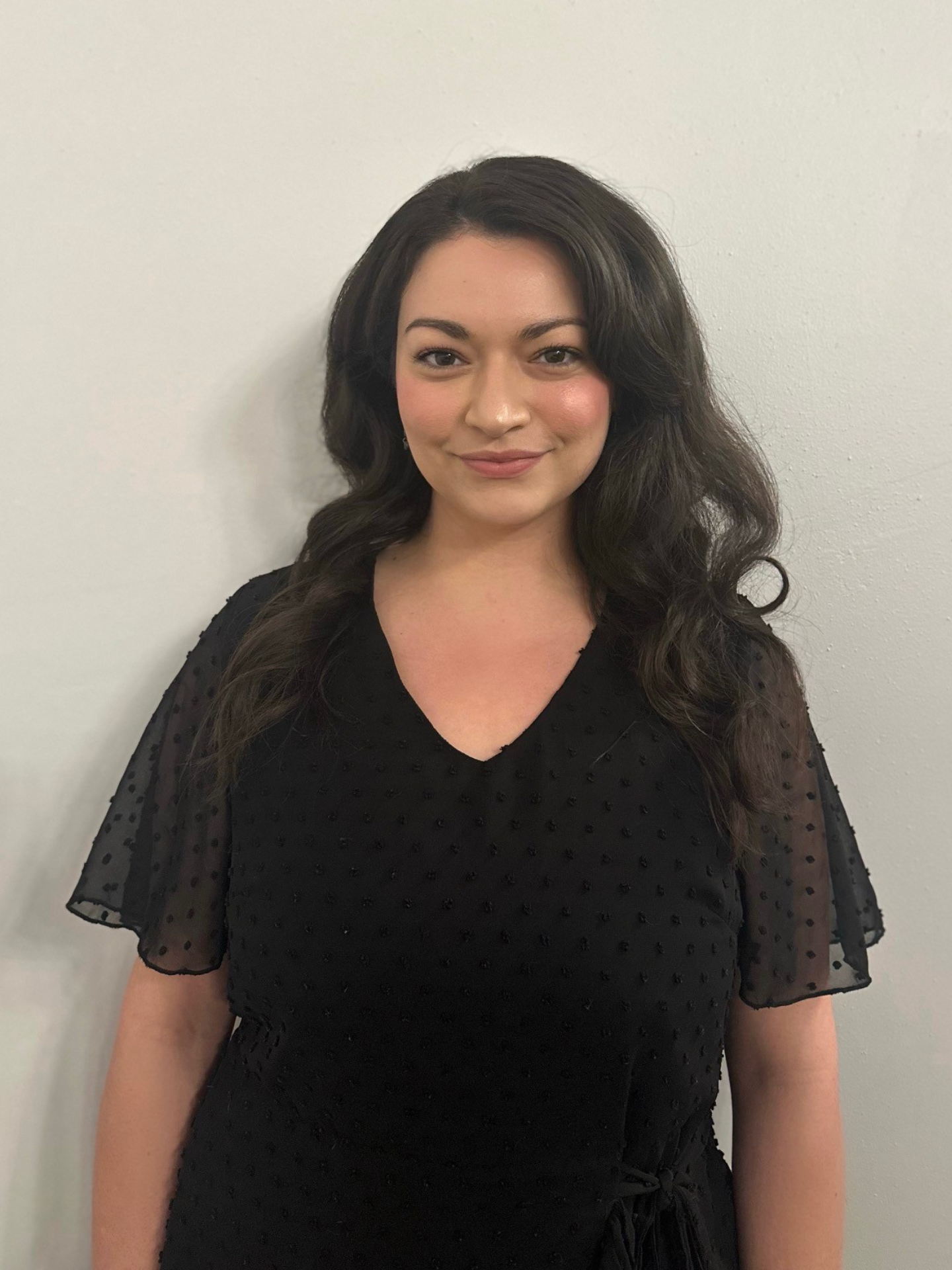 A woman in a black dress is standing in front of a white wall.