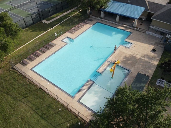 An aerial view of a large swimming pool next to a tennis court.