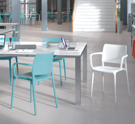 Area relax moderna in ufficio con sedie turchesi e bianche disposte attorno a un tavolo e una scala sullo sfondo.