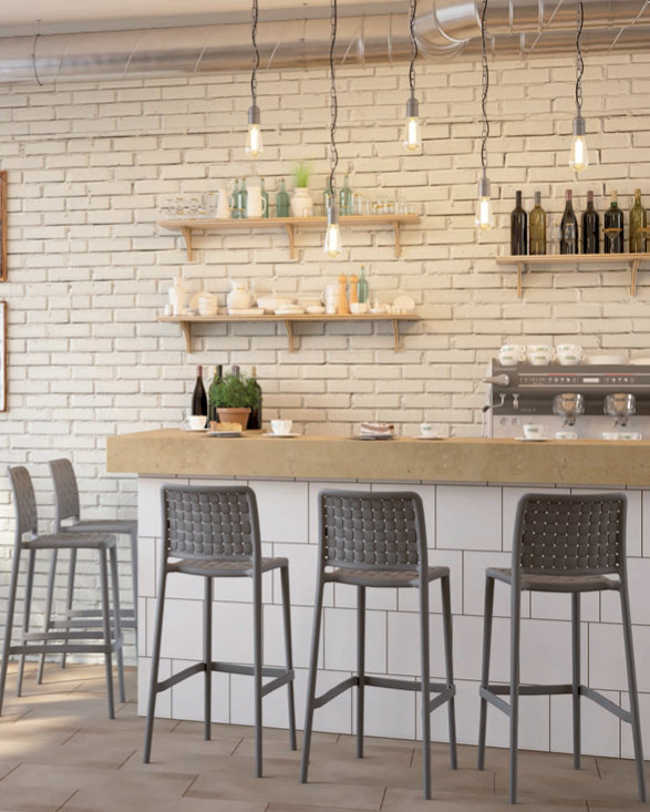 Caffè moderno con parete in mattoni bianchi, scaffali in legno e sgabelli grigi attorno a un bancone in legno.