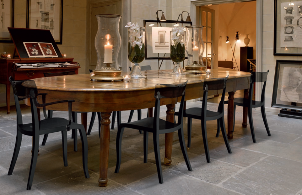 Tavolo da pranzo in legno con sedie nere in un interno rustico illuminato da luci soffuse, decorato con quadri e candele.