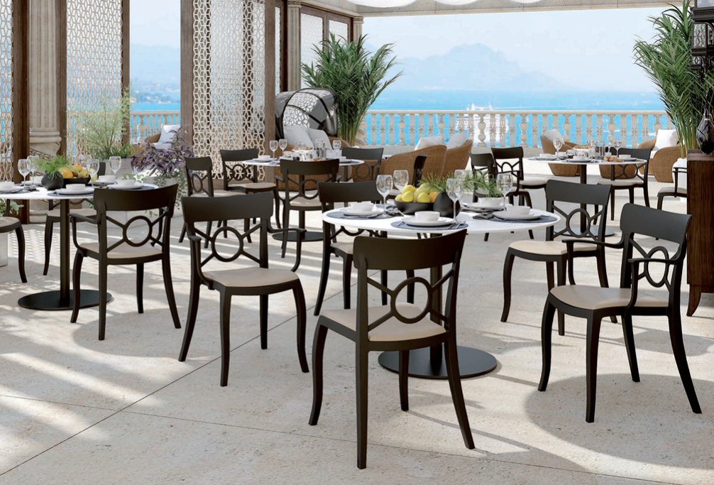 Terrazza esterna del caffè sul lungomare con tavoli e sedie neri, ideale per la colazione con vista sull'oceano.