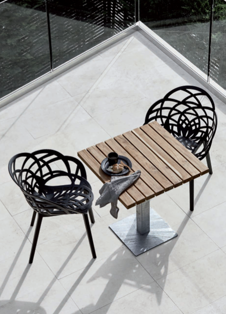 Tavolino da esterno con due sedie nere e tazza da tè su una terrazza piastrellata.