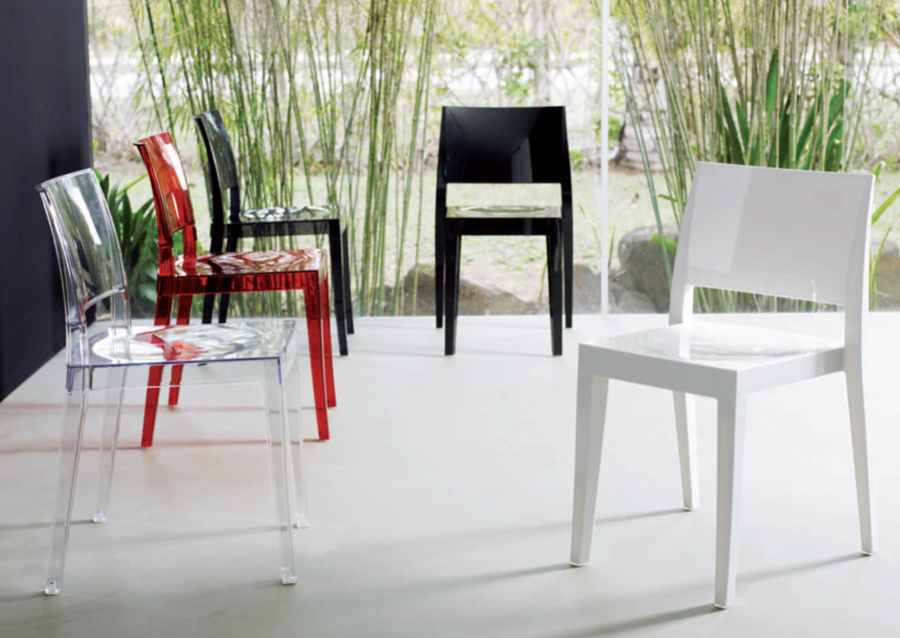 Sedie moderne nei colori nero, rosso, trasparente e bianco, disposte su un pavimento luminoso con bambù sullo sfondo.