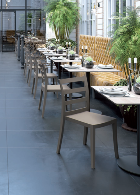 Terrazza esterna del ristorante con tavoli ben apparecchiati, sedie grigie e piante in vaso lungo un vialetto piastrellato.