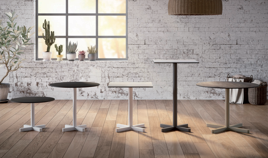 Interno moderno e minimalista con diversi tavolini e sgabelli da caffè su un pavimento in legno, accanto a una finestra luminosa.