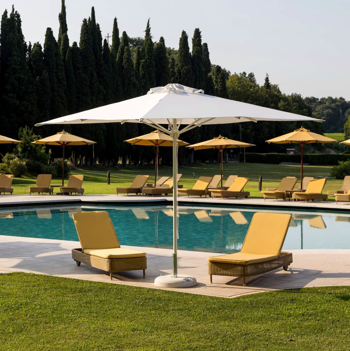 Piscina del resort con lettini e ombrelloni gialli accanto a un prato erboso e ad alti alberi.