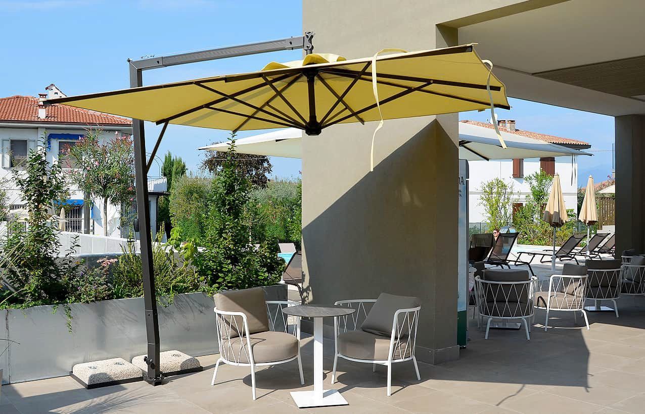 Dehor di un caffè all'aperto con ombrelloni gialli, sedie bianche e tavolini in un cortile soleggiato.