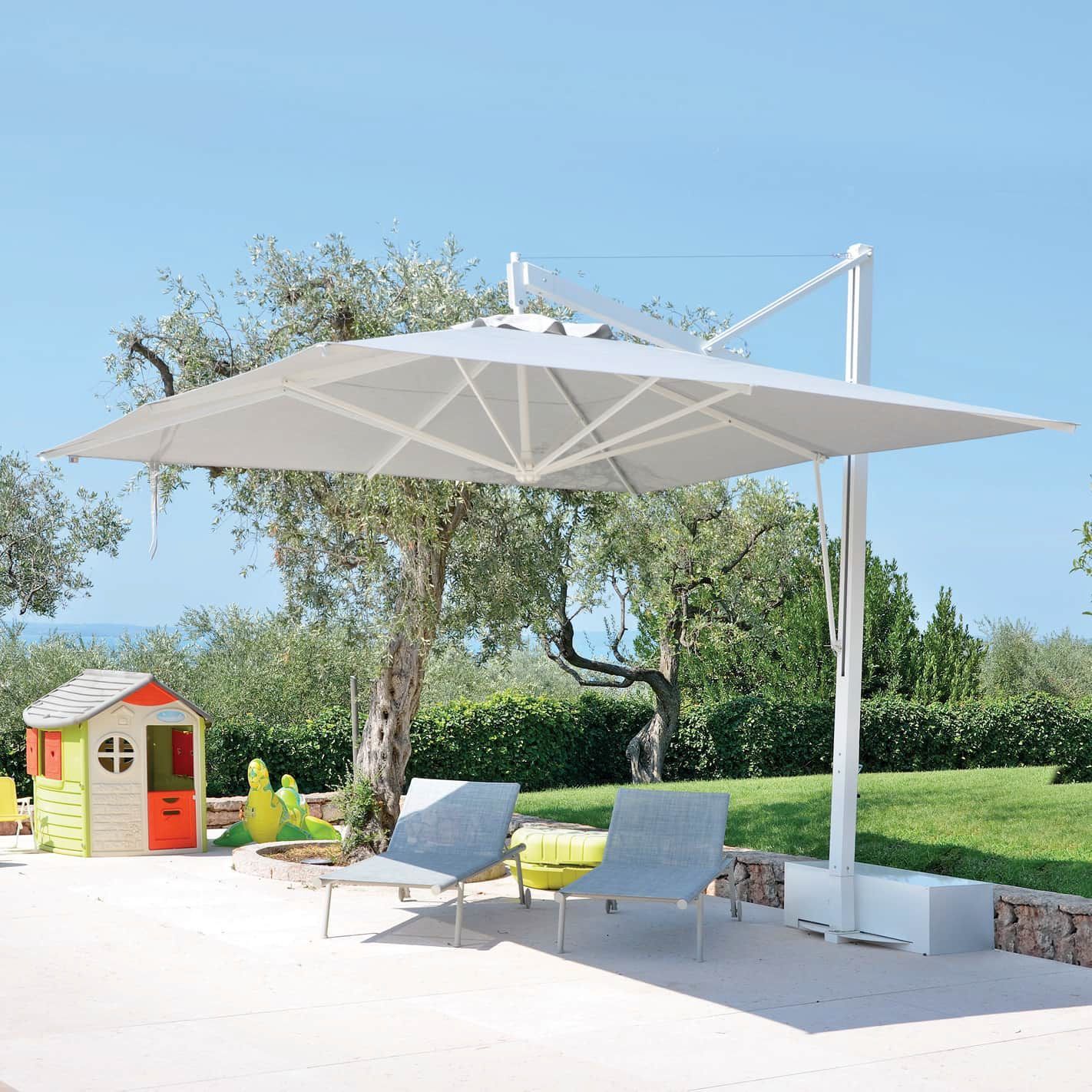Patio moderno con grande ombrellone bianco, due sedie a sdraio e una piccola casetta per bambini accanto a un prato verde.