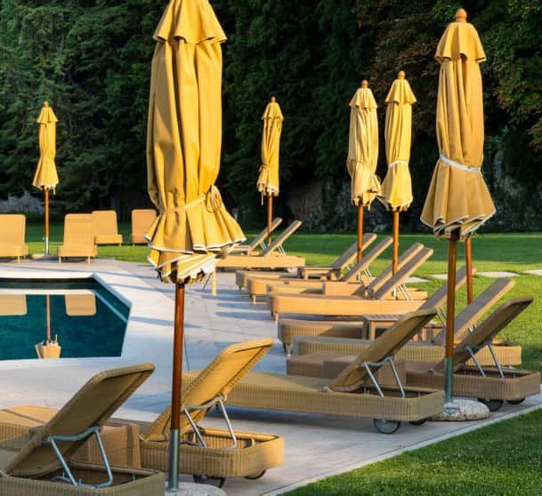 Sedie a sdraio gialle e ombrelloni chiusi a bordo piscina su un patio soleggiato.