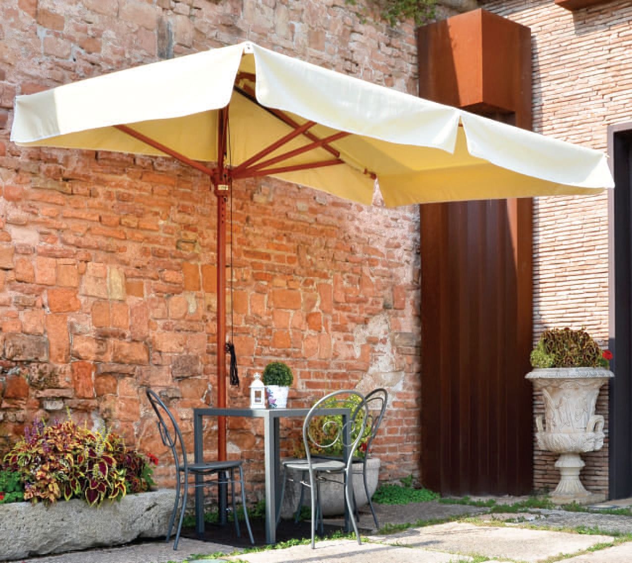 Tavolo da patio con ombrellone accanto a un muretto di mattoni e fioriera da giardino.
