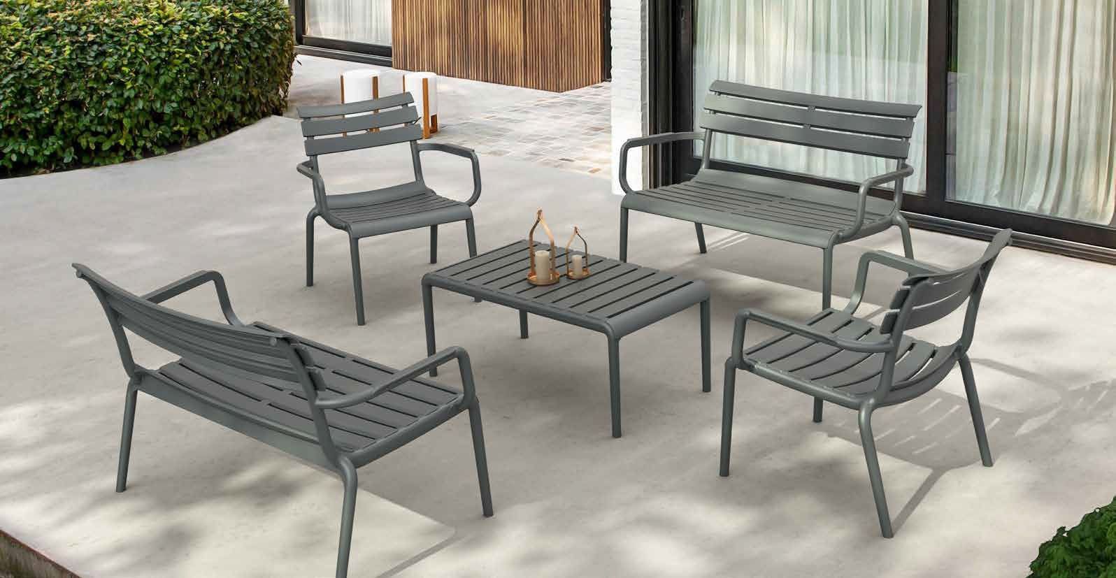 Arredamento da esterno per patio con sedie in metallo grigio, una panca e un tavolo quadrato su un patio in pietra chiara.