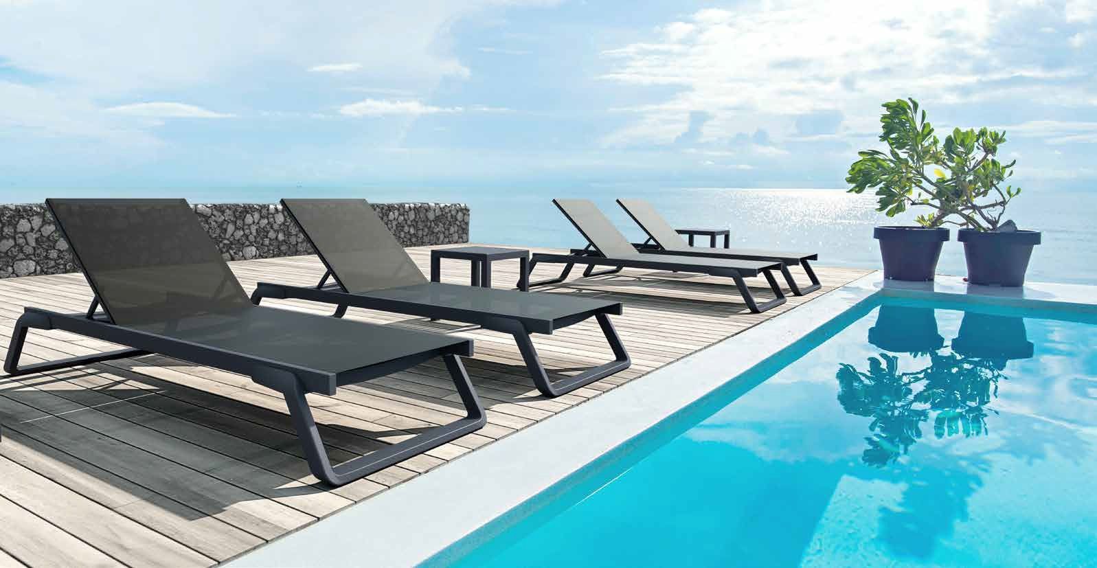 Moderna terrazza a bordo piscina con lettini neri accanto a una piscina di un blu brillante e piante in vaso.