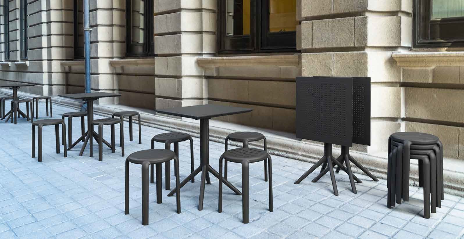 Tavolini e sedie da caffè all'aperto su un marciapiede pavimentato accanto a un edificio.
