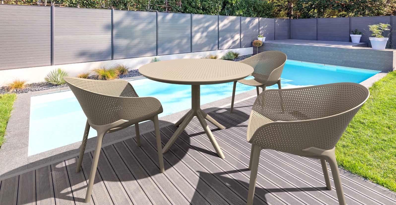 Patio esterno con tavolo rotondo e quattro sedie in vimini accanto a una piscina e al prato.