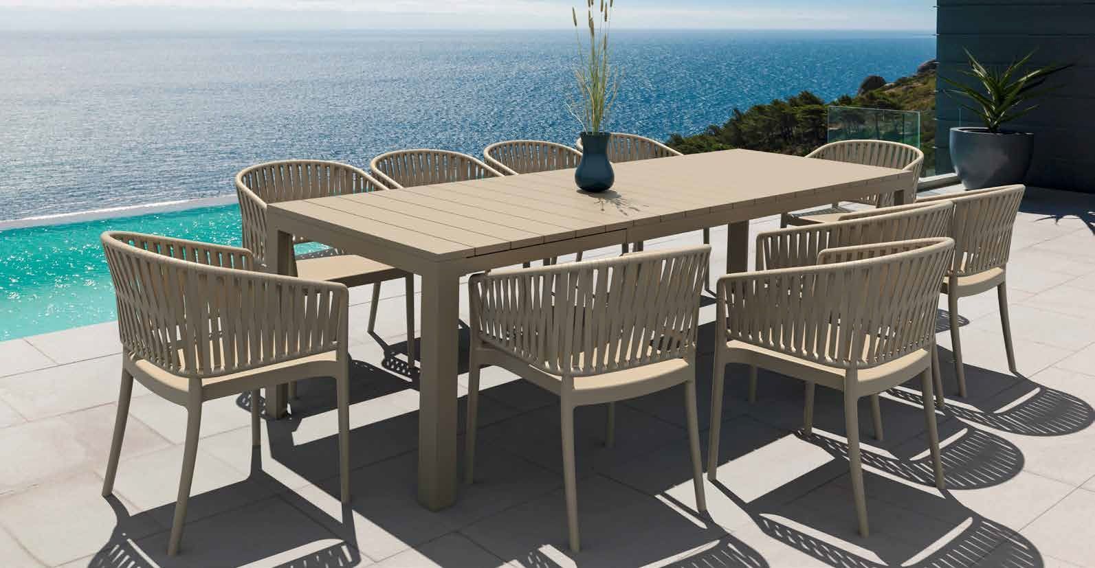 Set da pranzo da esterno con sedie e tavolo beige con vista su un oceano turchese e un cielo azzurro.